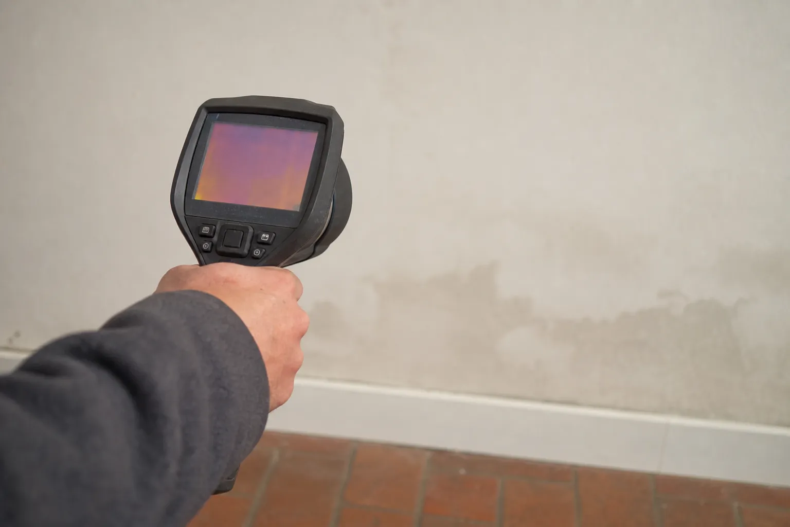 Caméra thermique portative tenue face à un mur intérieur clair marqué d’une auréole d’humidité